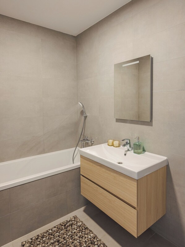 A modern bathroom with a freestanding bathtub, a vanity with a mirror, and a small rug on the floor.