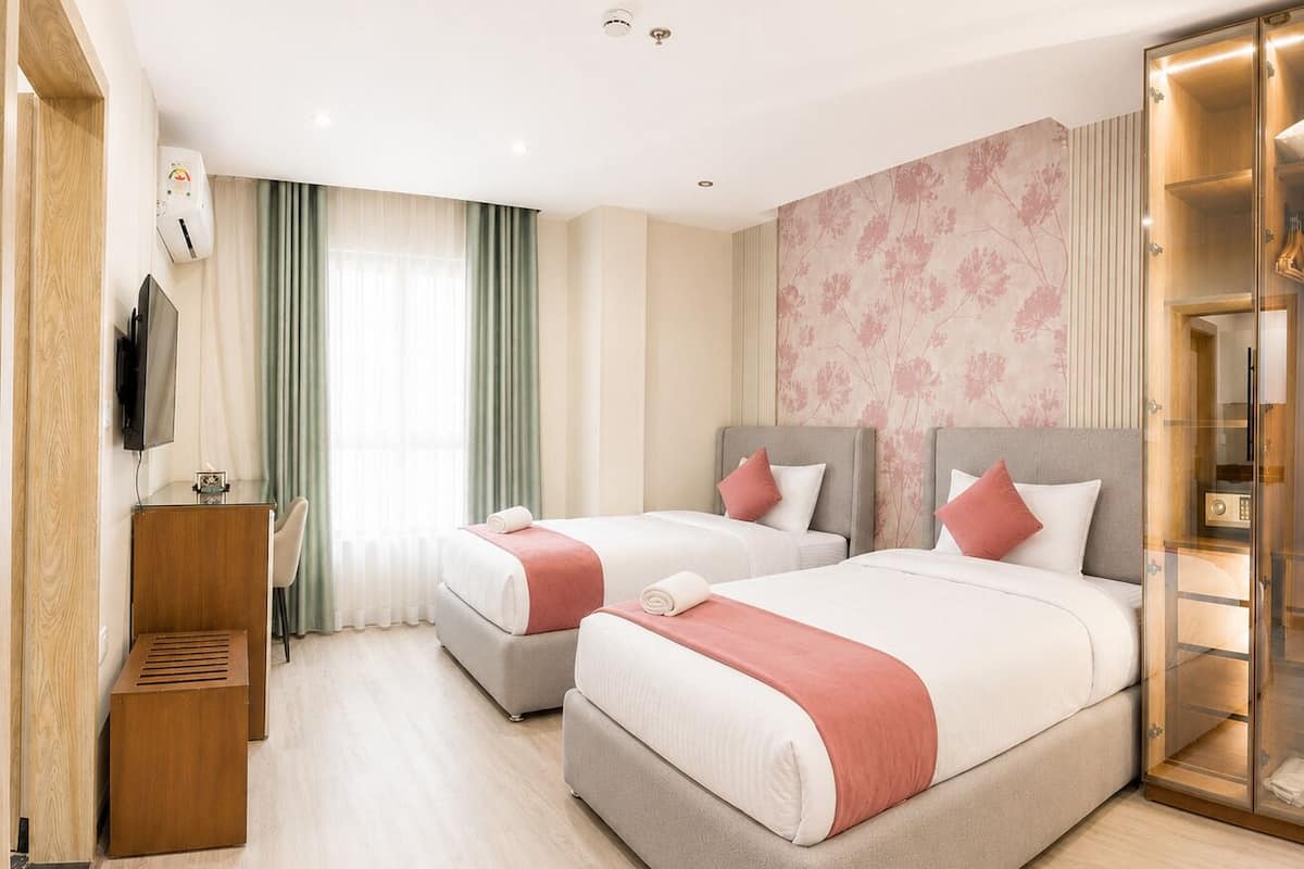 A hotel room with two beds, a TV, a desk, and a glass-enclosed bathroom.
