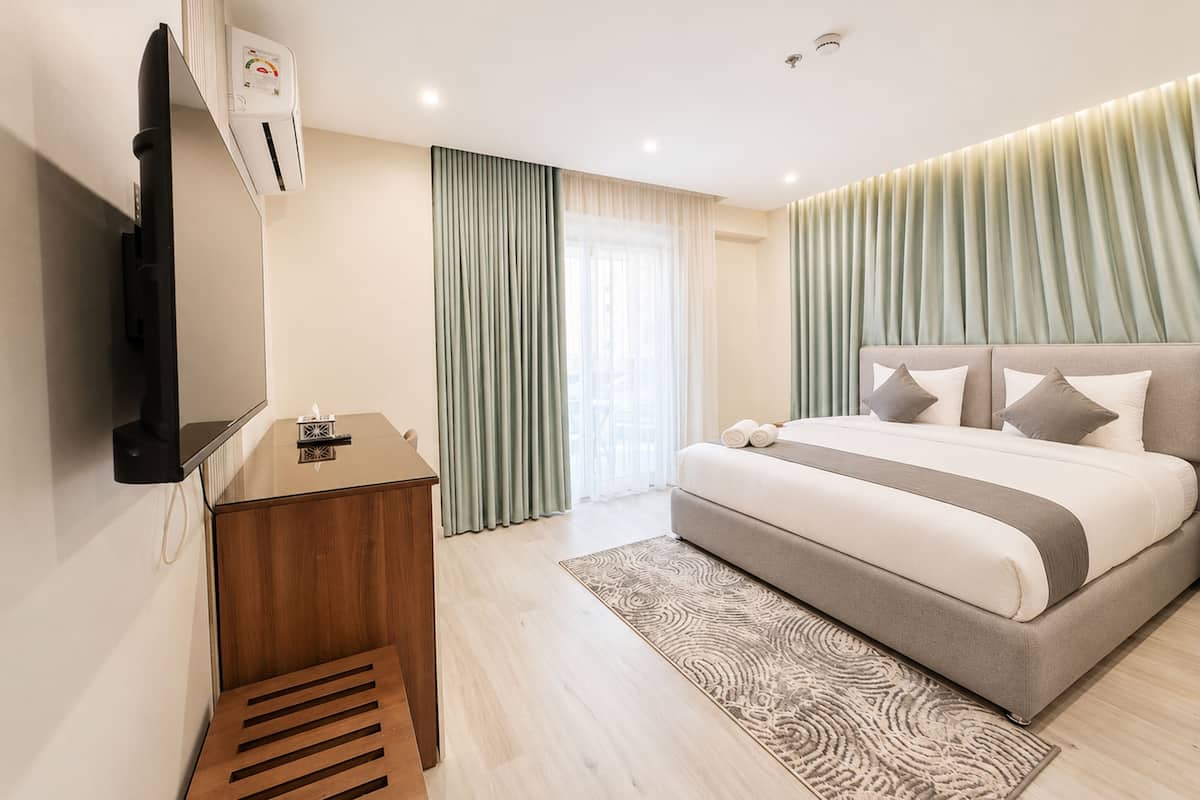 A modern hotel room with a bed, bedside table, TV, and a view of the city.