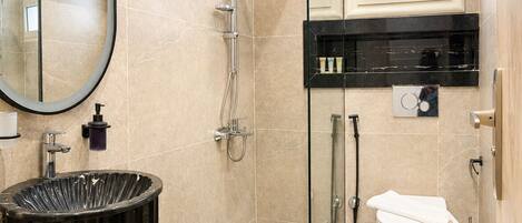 A modern bathroom with a glass-enclosed shower, a black sink, a toilet, and a mirror.
