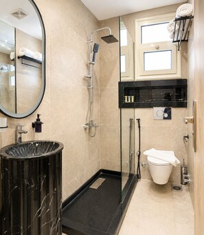A modern bathroom with a glass-enclosed shower, a black sink, a toilet, and a mirror.