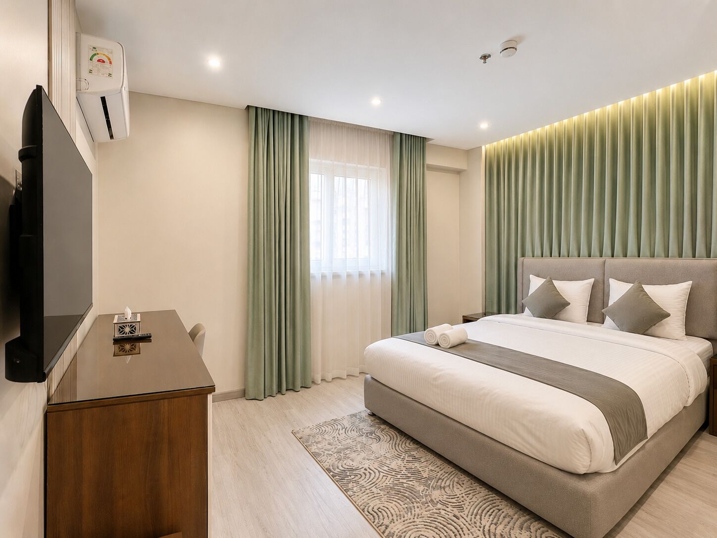 A modern hotel room with a bed, a TV, a desk, and a window with curtains.
