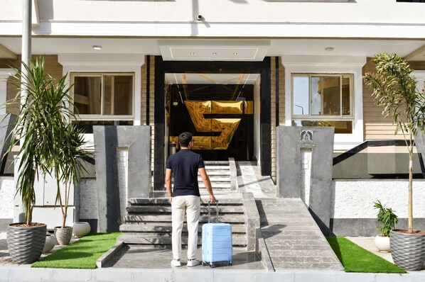 A man with a suitcase at the entrance of a building with a large, abstract sculpture.