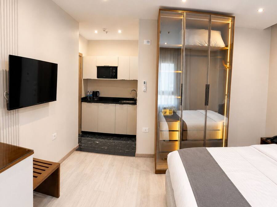 Ein kleines Hotelzimmer mit Bett, Fernseher, einer Küchenzeile und einem Schiebetürenschrank.