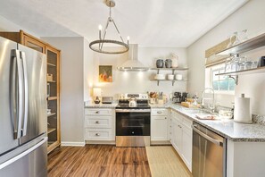 Une cuisine moderne dotée d’appareils électroménagers en acier inoxydable, d’un plancher en bois et d’un lustre.