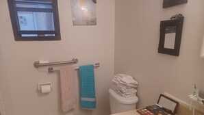A bathroom with a toilet, a sink, a towel rack with towels, a stack of folded towels, a window, and a mirror. - Spacious renovated 2 1/2 sleeps 3 (Montréal)