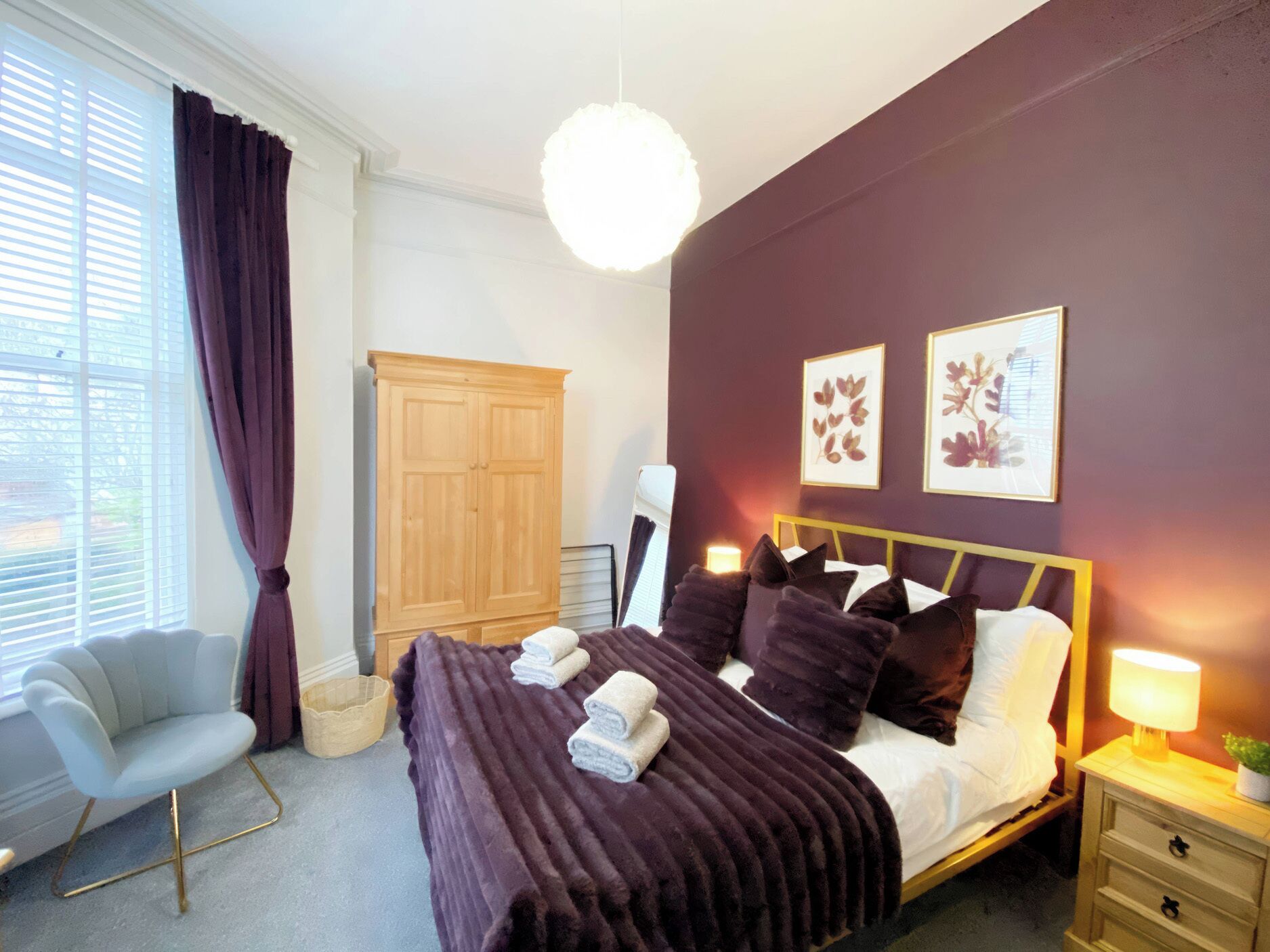 Un dormitorio con cama, una silla, un armario y obras de arte en la pared.