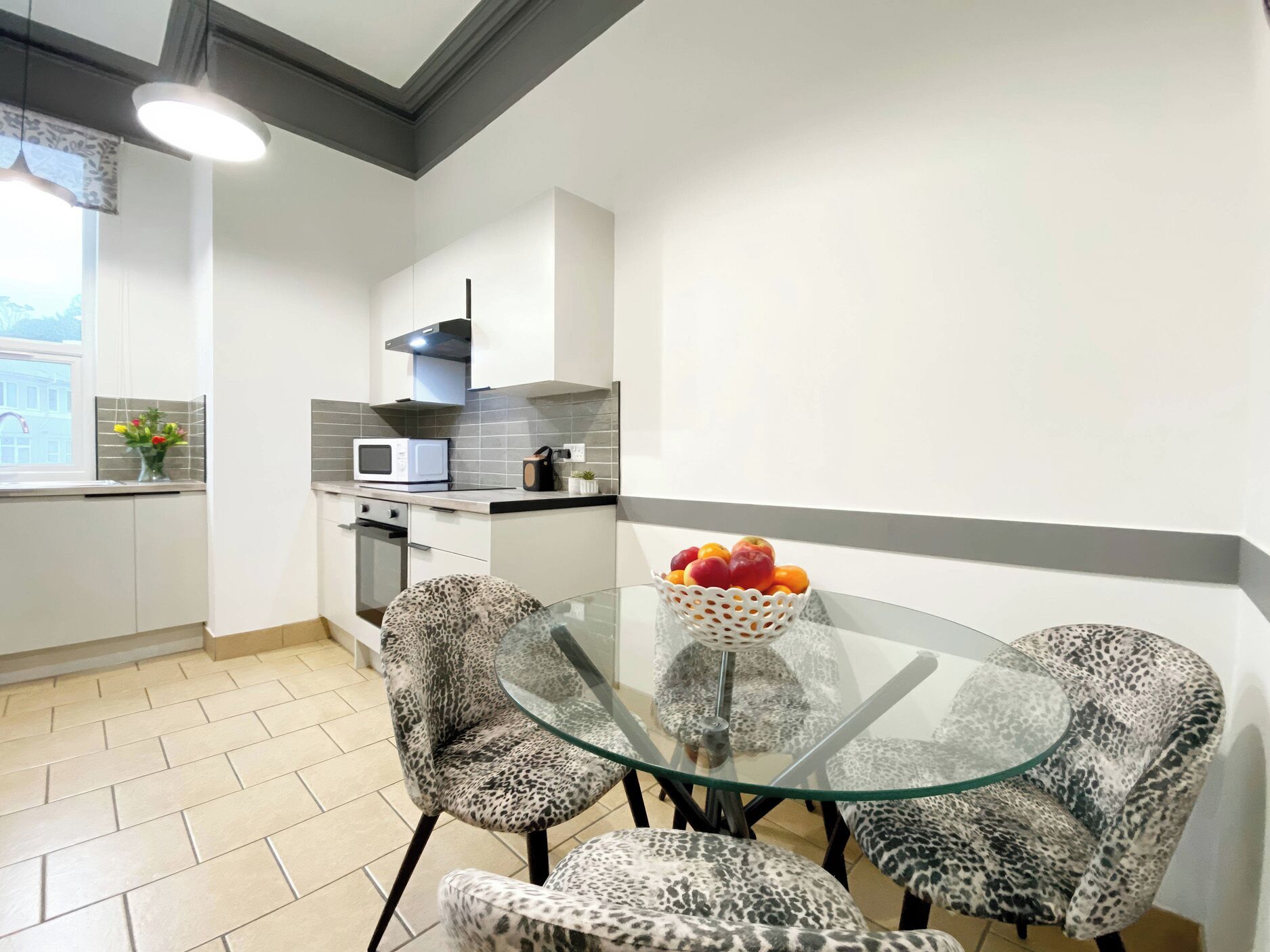 A modern kitchen with white cabinets, a microwave, and a glass table with leopard print chairs.