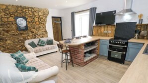 A modern kitchen with a built-in stove, a dining area with a white sofa and a stone wall. - Woodpecker (Haverfordwest)