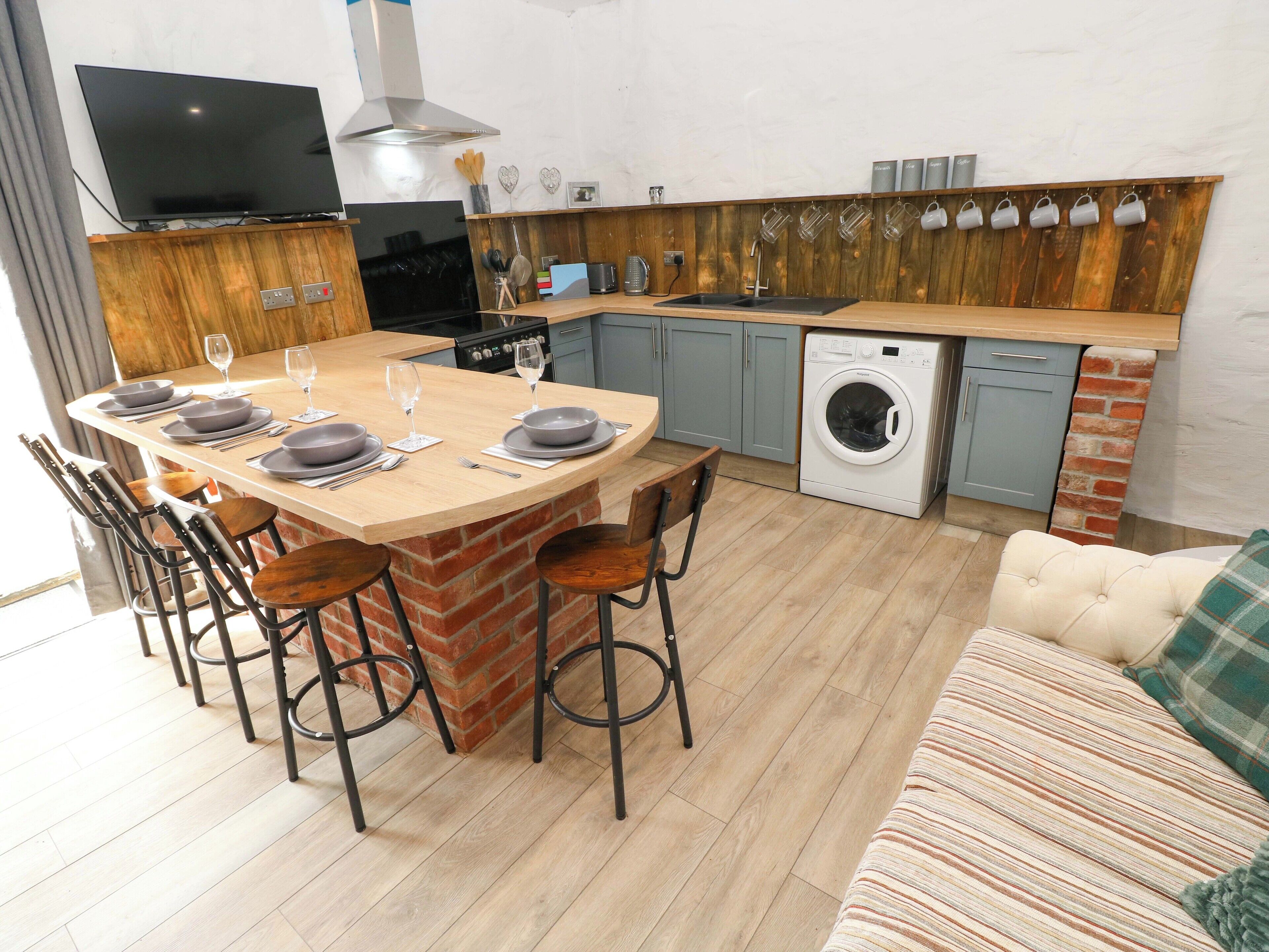 Een moderne keuken met een centraal eiland, barstoelen, een ingebouwde wasmachine en een flatscreen televisie.