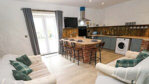 A modern living room with a sofa set, a dining area with a brick island, and a kitchen with a washing machine. - Woodpecker (Haverfordwest)