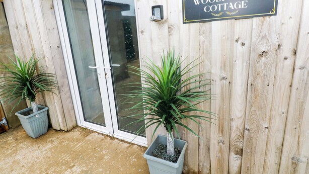 A wooden cottage with a sliding glass door and two potted plants. - Woodpecker (Haverfordwest)