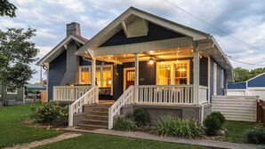 Ein zweistöckiges Haus mit Veranda, Treppe und gepflegtem Rasen.