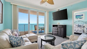 A room with a sofa, a small table, a cabinet, a TV, and a balcony with a view of the ocean. - Gulfview Haven by Avantstay Beachfront Condo + Pool + Hot Tub + Spa + Near Pier Park (Panama City Beach)