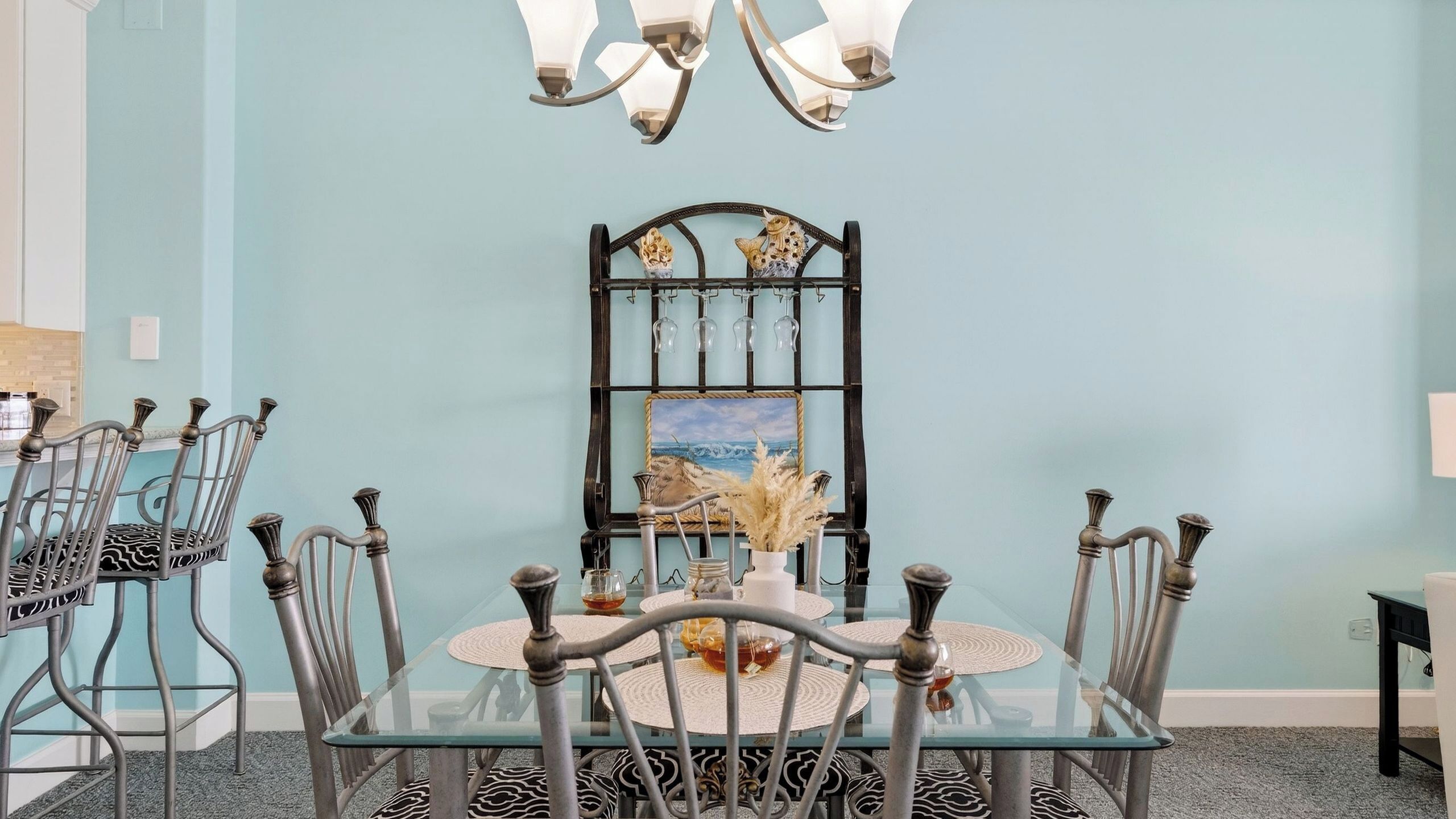Un coin repas avec une table en verre, des chaises en métal, un lustre et un tableau au mur.