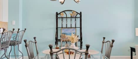 Un comedor con una mesa de vidrio, sillas de metal, una araña y un cuadro en la pared.