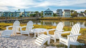A beach with white Adirondack chairs and a small table, a wooden pier, and houses in the background. - BEACH THERAPY: Lovely Spacious and Comfortable Coastal Family Retreat (Rockport)