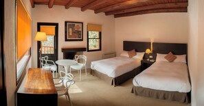 A hotel room with two beds, a small table, chairs, a fireplace, and a window with blinds. - Postales (Chacras de Coria)