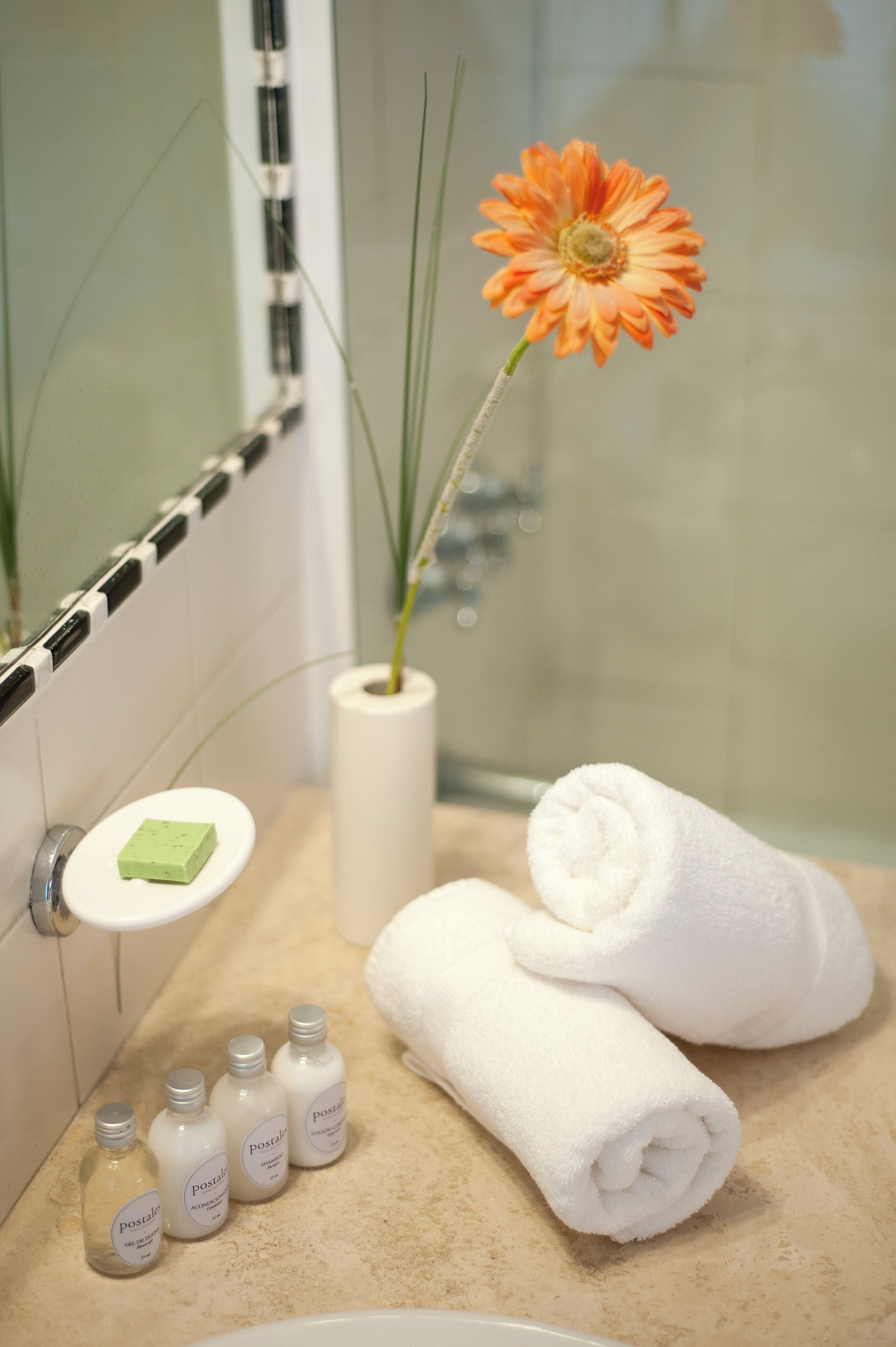A bathroom with a sink, a toilet, a towel, a flower, and toiletries.
