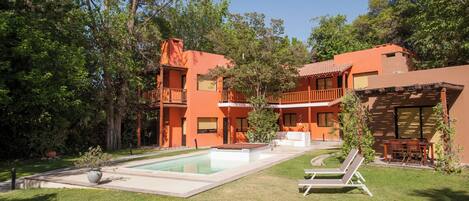 A two-story building with a swimming pool, outdoor seating, and lush greenery.