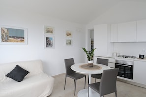 A modern kitchen with white cabinets, a round dining table, and a sofa with a black cushion.