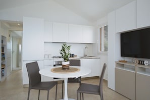 Una cocina moderna con armarios blancos, una mesa de comedor con sillas y un televisor en la pared.