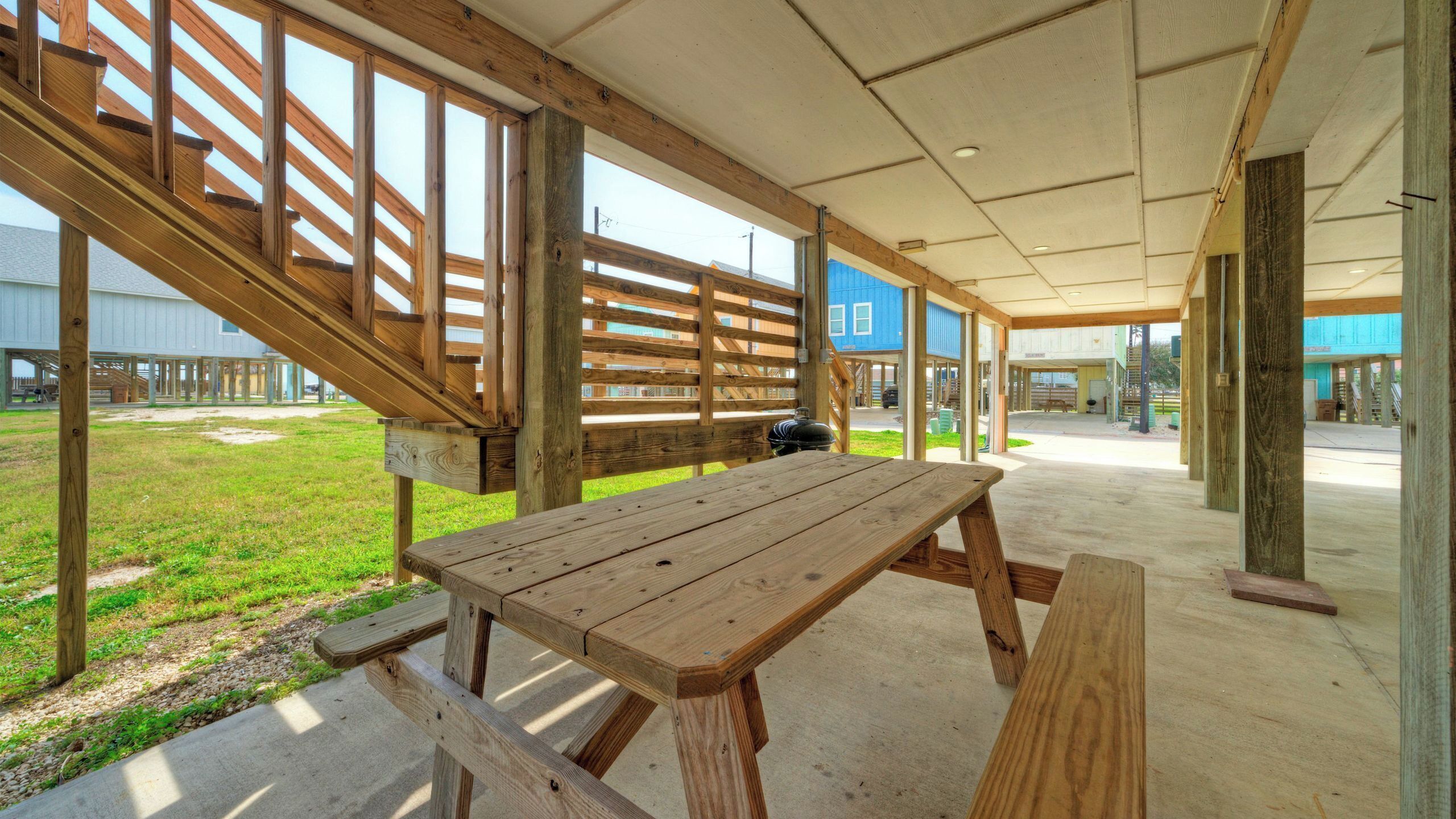 Un espacio al aire libre techado con una mesa de picnic y bancos, barandas de madera y vistas del entorno.