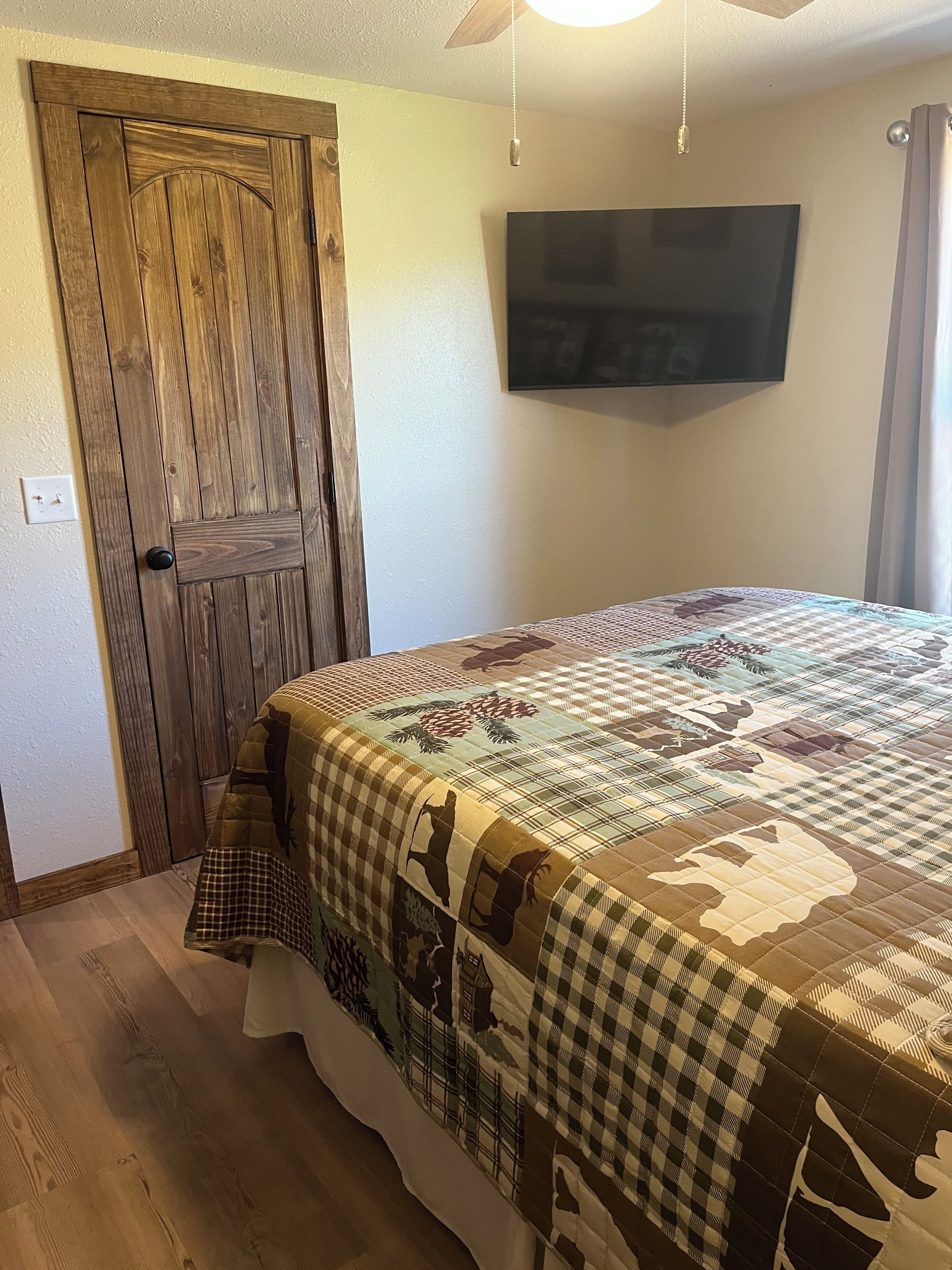 Un dormitorio con puerta de madera, una cama con colcha, un televisor de pantalla plana y un ventilador de techo.