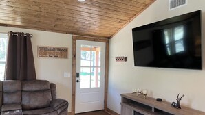 Ein Wohnzimmer mit braunem Ledersofa, einem flachbildfernseher an der Wand, einer Holz-Unterhaltungsecke und einer Tür mit Glasfenster.