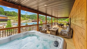 Ein überdachter Außenbereich mit Whirlpool, Korbmöbeln und Blick auf Pool und Landschaft.
