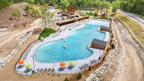 Ein großer, gewölbter Swimmingpool mit Liegestühlen und Sonnenschirmen, umgeben von einer Steinmauer und einem Gebäude mit Holzveranda.