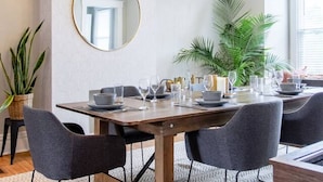 A dining area with a wooden table, grey chairs, a round mirror, and a ceiling light fixture. - Spacious 5BR Home | Great for Groups & Families (Pittsburgh)