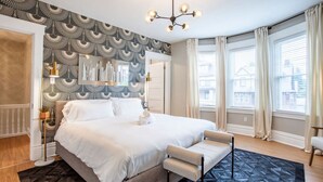 A bedroom with a large bed, a bedside table, a chair, and a patterned wallpaper. - Spacious 5BR Home | Great for Groups & Families (Pittsburgh)
