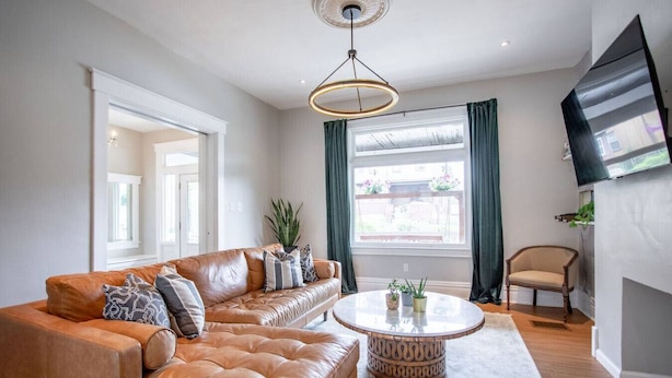 A modern living room with a leather sofa, a round coffee table, and a flat-screen TV mounted on the wall. - Spacious 5BR Home | Great for Groups & Families (Pittsburgh)