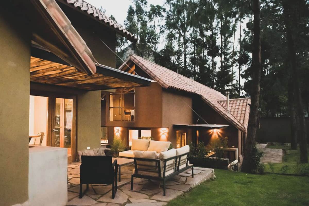 A modern house with a patio area, outdoor seating, and a view of the surrounding forest.