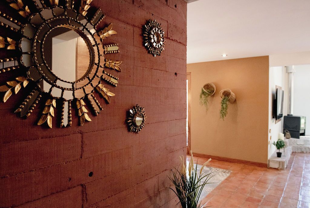 Une pièce avec un mur en briques, un grand miroir orné d’un motif en forme de soleil, et deux objets décoratifs fixés au mur.