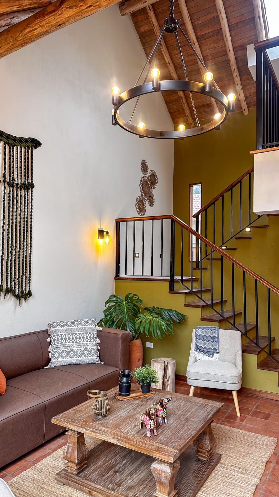 A cozy living room with a brown sofa, a wooden coffee table, and a staircase with a wooden railing.