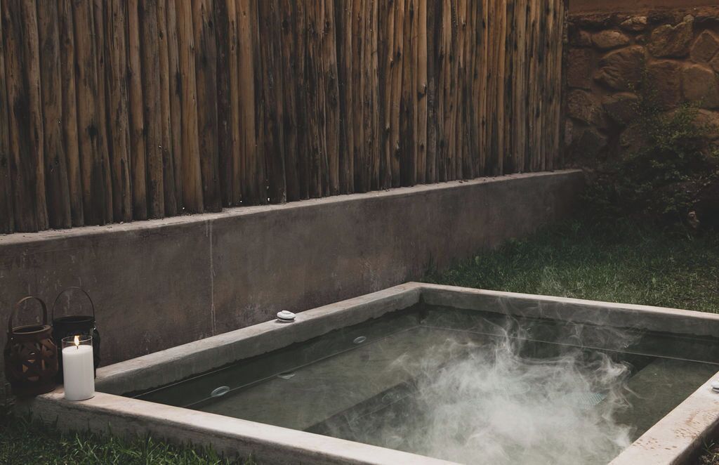 A hot tub with steam rising, surrounded by a concrete edge and a wooden fence.