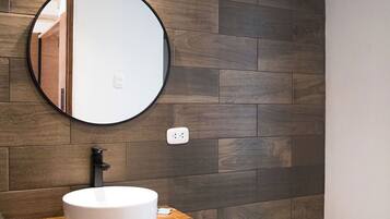 A modern bathroom with a round mirror, wooden vanity, white sink, and toilet.