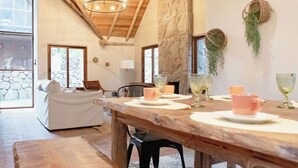 Una zona de menjador acollidora amb taula de fusta preparada per a quatre persones, paret de pedra i una planta penjant.