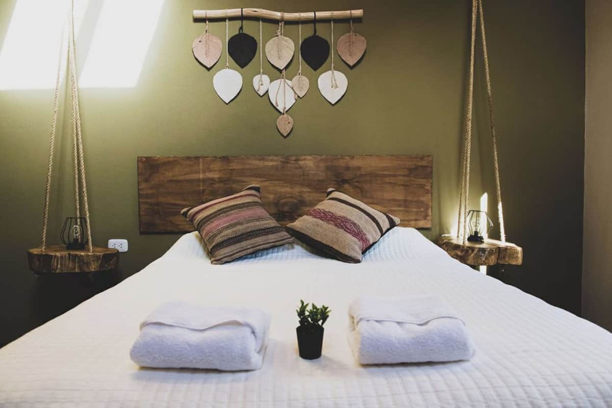 A neatly made bed with two pillows, a small potted plant, and a wall-mounted heart-shaped decoration.