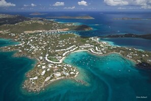 Vista aérea de un complejo turístico costero con varios edificios, aguas turquesas cristalinas y un puerto deportivo con barcos.