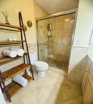 Un baño con ducha, inodoro y estantes de madera con toallas.