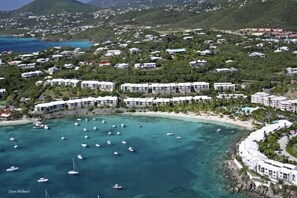 An aerial view of a coastal resort with multiple white buildings, a sandy beach, and clear turquoise waters with boats. - New High End Rental At Cowpet Bay! Amazing Views/Breezes! (East End)