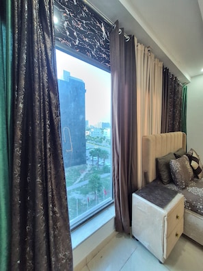 A bedroom with a large window, a bed with a headboard, and a nightstand.