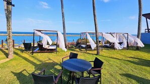 Un salon de plage avec des espaces de détente en plein air, comprenant une table et des chaises, ainsi que des hamacs sous des auvents blancs.