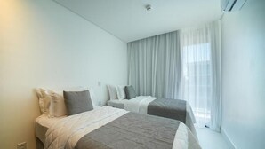 Une chambre d’hôtel avec deux lits, une grande fenêtre avec des rideaux légers et un climatiseur fixé au plafond.