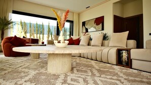 Un salon moderne avec une table basse ronde, des canapés de couleur beige et une grande fenêtre donnant sur un paysage arboré.