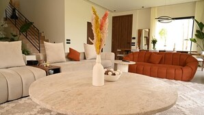 Een moderne woonkamer met een ronde salontafel, beige banken en een groot raam.