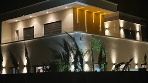 Een modern huis met twee verdiepingen, een balkon, inbouwspots en een grote verlichte muur.
